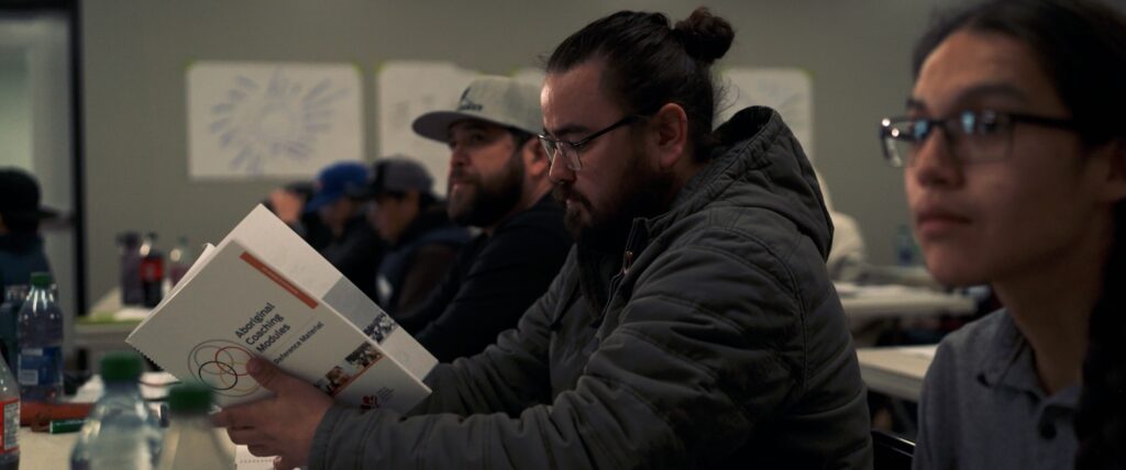 Coach reading Aboriginal Coaching Module book in classroom.