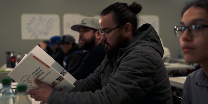 Coach reading Aboriginal Coaching Module book in classroom.